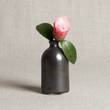 Simple metallic black porcelain bud vase holding a pink flower and green leaves.