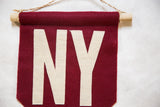 Hand-stitched cream 'N' letter on crimson felt, with visible wooden dowel and rope.