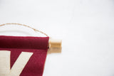 Close-up of crimson felt flag's hand-sewn cream letter, oak dowel, and jute string.