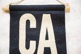 Navy felt CA flag with cream hand-sewn letters, wooden dowel, and twine.