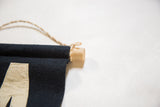 Detail of navy felt flag showing oak dowel, jute twine, and cream letter stitching.
