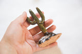 Hand holds the dark ceramic cactus, with glossy glaze and speckled clay base.