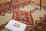 Distressed antique Malayer rug detail: red quatrefoil designs in a diamond medallion on a camel field.