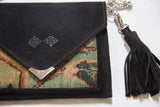 Close-up of the black suede flap with embossed logo, metal corner, and tassel.