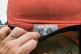 Brand label with green logo inside the bag's textured orange vegetable suede flap.