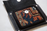 Geometric hand-knotted rug fragment in rust, blue, and sage green, with black suede trim.