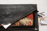Embossed logo and silver corner on the textured black flap of the handmade rug fragment clutch.