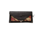 Black vegetable suede flap with an embossed logo and metal tip on a rug clutch.