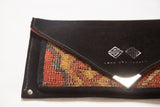Black suede clutch detail with Swag and Tassel logo, vibrant red and gold rug fragment.
