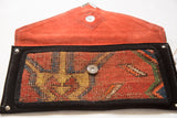 Open handmade clutch displaying rich orange suede lining and patterned rug fragment.