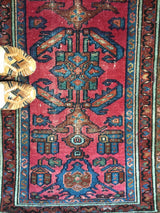 Distressed ruby red pile with blue geometric patterns on an antique Lilihan rug.