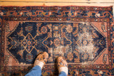 Decorative distressed texture on an antique rug showing faded Herati pattern in navy and dusty rose.