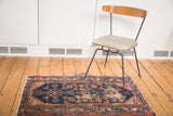 Distressed Malayer rug section, revealing faded navy, dusty rose, and ivory Herati patterns.