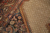 Finely serrated border of a distressed Hamadan rug in rust, blue, green, on a camel field.