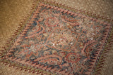 Distressed Persian Hamadan rug detail, showing a prominent hole among blush, navy, and camel motifs.