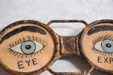 Vintage Eyeglass Sign: hand-painted blue eye and 'EYE' text on rusted metal frame.