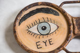 Vintage Eyeglass Sign with blue painted eye, black lashes, 'EYE' text, and rusted frame.