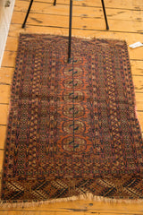 Distressed Turkmen rug with repeating Bokhara gul design in faded reds and navy tones.