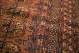 Distressed pile of the Turkmen Bokhara rug with faded raspberry, rust, and navy geometric pattern.