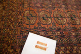 Distressed vintage Turkmen rug with repeating gul Bokhara pattern in faded raspberry, rust, and navy.