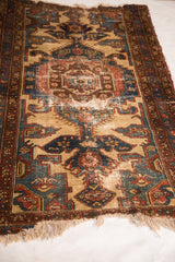 Tattered fringe and distressed texture of a vintage Malayer rug with camel, red, and blue.