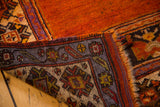 Folded corner of vintage Oushak rug, showing tangerine orange field and geometric purple border.