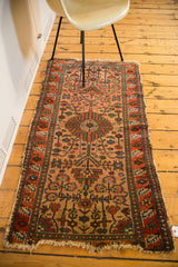 Malayer rug corner with dusty blush rose field, geometric tendrils, and tattered fringe.