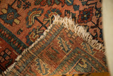 Folded vintage Malayer rug corner with natural worn fringe and visible geometric backweave.