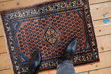 Small Engelas rug mat shown for scale, featuring a terracotta field and blue geometric design.