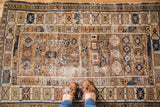 Antique distressed Caucasian Kuba rug corner with geometric indigo, orange, and earthy patterns.