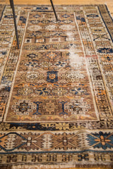 Antique Caucasian rug's detailed geometric border, worn fringe, and varied blue and orange tones.