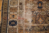 Distressed weave of an antique Caucasian rug with geometric indigo, tangerine, and ivory motifs.