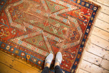 Antique Sewan Kazak rug displaying distressed texture, fragmented shield designs in madder red, olive, and blue.