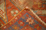 Folded corner of an antique Sewan Kazak rug, showing madder red field, blue border star motif, and distressed pile.
