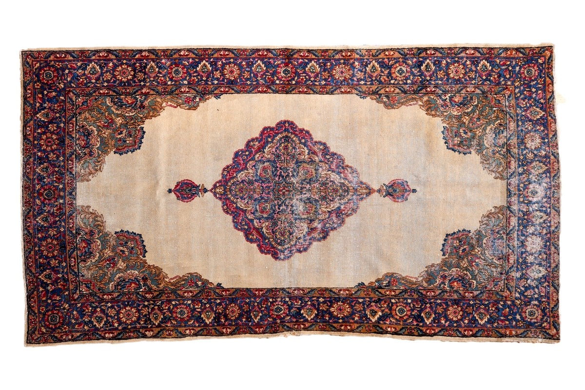 Distressed Kerman rug with scalloped medallion, rococo leaves, ivory field, and milfleur border.