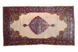 Distressed Kerman rug with scalloped medallion, rococo leaves, ivory field, and milfleur border.
