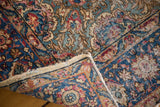 Distressed Kerman rug corner reveals worn texture, intricate floral motifs, colorful pile, and fringe.