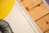 Poster detail showing bright yellow, off-white, English and Cyrillic text, and linen mount edge.