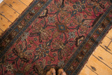 Angled view of vintage Lilihan rug corner, ruby rose field, teal border, tattered edge.