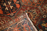 Folded corner of antique distressed Baktiari rug, revealing hand-knotted fringe and geometric details.