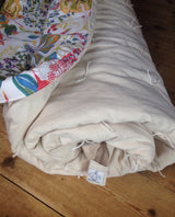 Rolled handmade sleeping bag with colorful floral print lining and natural beige exterior.