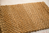 Textured golden surface of a hand woven hemp and jute entrance mat.