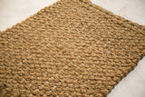 Hand braided entrance mat showing tight woven texture and natural golden fibers.