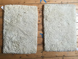 Two plush, hand-knotted Moroccan shag bath rugs with soft off-white pile, 2x3 size.