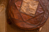Vintage leather pouf top featuring brown patchwork, central de-haired hide, and aged seams.