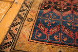Antique Malayer rug corner showing geometric border patterns in deep blue, terracotta, and ochre.