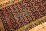 Malayer rug corner detail, showing dark field's geometric motifs, ochre border, and foundation wear.