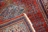 Folded corner of Persian style Mir Serbend rug, revealing red rust field botehs, blue mirror border, and ivory fringe.