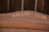 Faded gold Kiwanis Club lettering on curved brown wood vintage display.