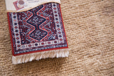 Vibrant red, navy, and cream geometric patterns on a miniature Qashqai carpet coaster.